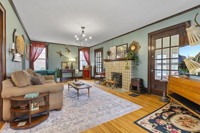 living room with crown molding, hardwood / wood-style floors, a tile fireplace, and a notable chandelier