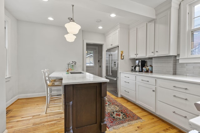 kitchen featuring sink, light hardwood / wood-style flooring, high end fridge, white cabinets, and decorative light fixtures