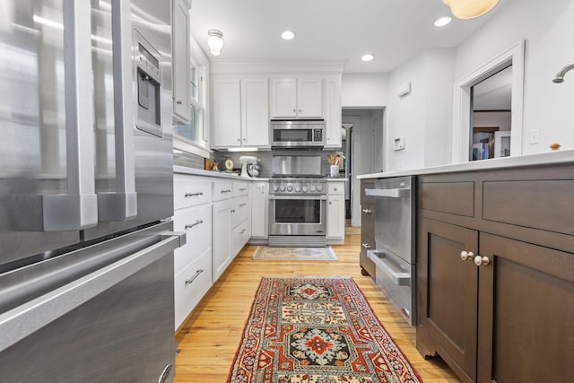 kitchen featuring stainless steel appliances, white cabinetry, light hardwood / wood-style floors, and decorative backsplash