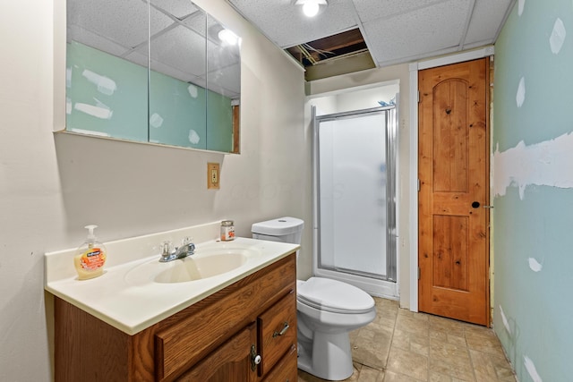 bathroom featuring vanity, toilet, a shower with shower door, and a drop ceiling