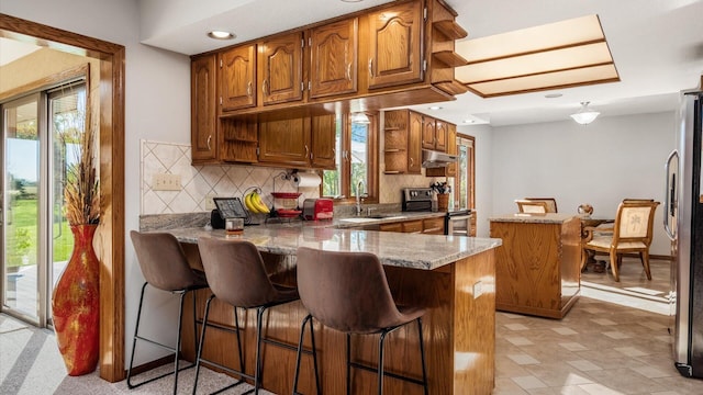 kitchen with appliances with stainless steel finishes, tasteful backsplash, a kitchen bar, light stone counters, and kitchen peninsula