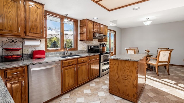 kitchen featuring sink, appliances with stainless steel finishes, a center island, light stone counters, and tasteful backsplash