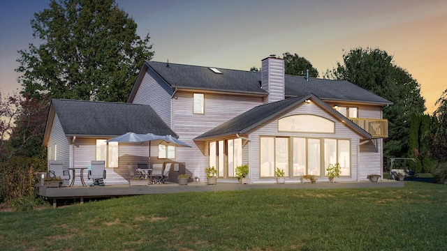 back house at dusk featuring a yard and a deck