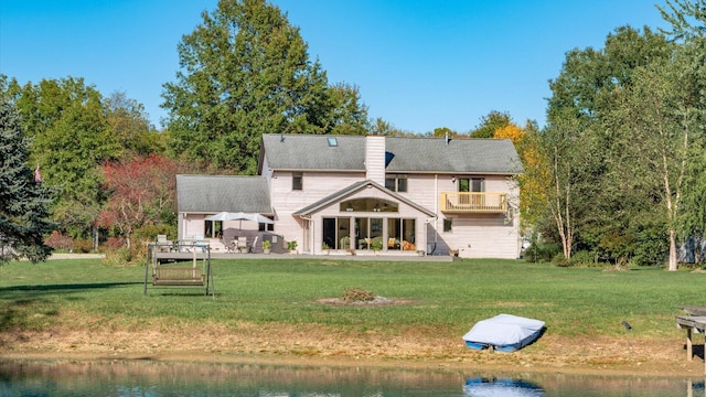 rear view of house featuring a balcony, a water view, a patio area, and a lawn