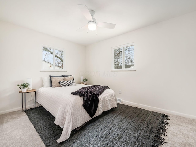 bedroom with ceiling fan, multiple windows, and dark colored carpet