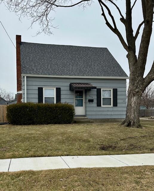 view of front of home featuring entry steps, a shingled roof, a chimney, and a front yard