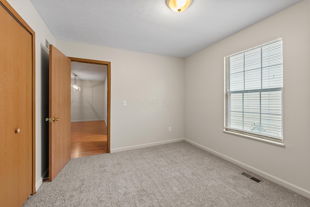 unfurnished bedroom featuring light colored carpet, a closet, and a textured ceiling