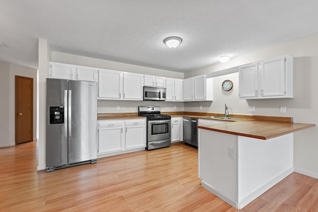 kitchen featuring sink, white cabinetry, stainless steel appliances, light hardwood / wood-style floors, and kitchen peninsula