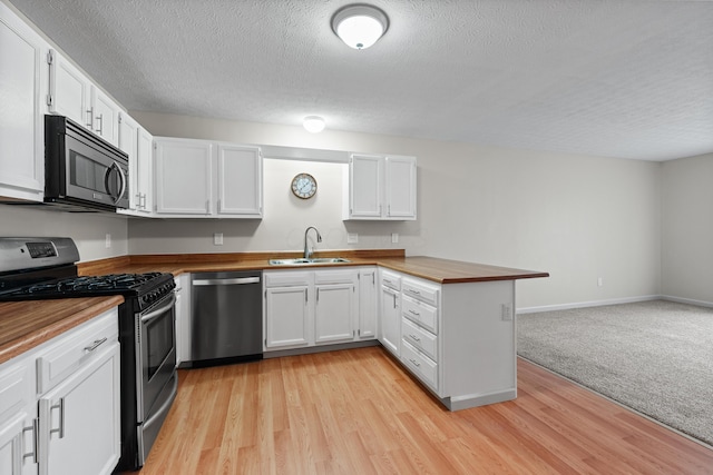 kitchen featuring appliances with stainless steel finishes, sink, wooden counters, white cabinets, and kitchen peninsula