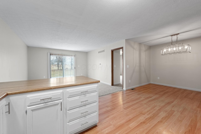 kitchen with light hardwood / wood-style flooring, hanging light fixtures, a textured ceiling, white cabinets, and a chandelier