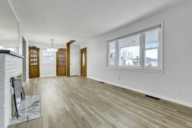 unfurnished living room with an inviting chandelier, a fireplace, and light hardwood / wood-style floors