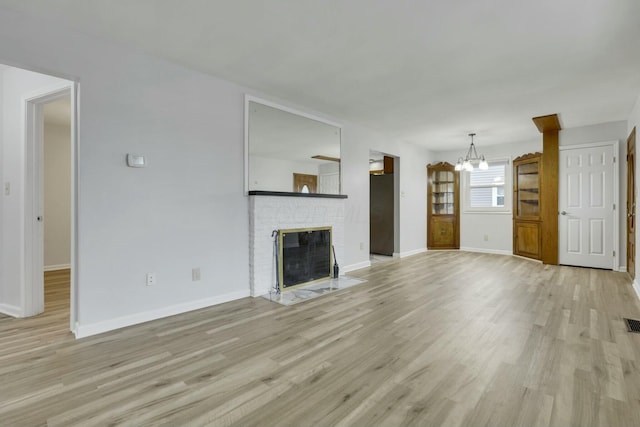 unfurnished living room with light hardwood / wood-style floors, a brick fireplace, and a notable chandelier