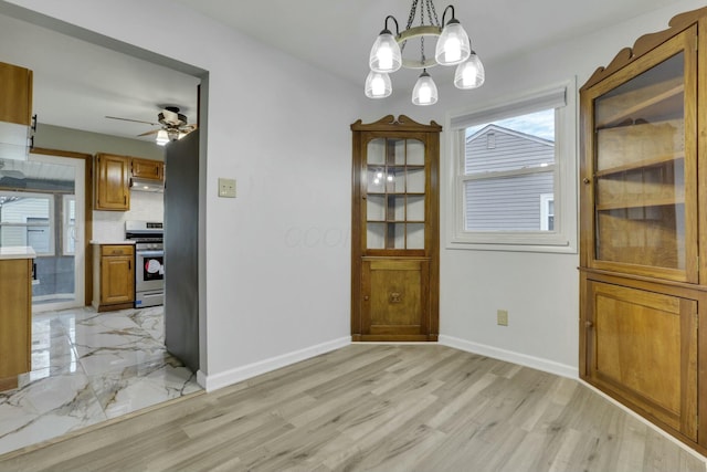 unfurnished dining area featuring ceiling fan with notable chandelier and light hardwood / wood-style flooring