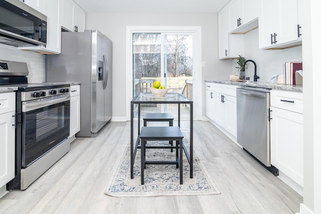 kitchen with appliances with stainless steel finishes, white cabinetry, sink, backsplash, and light stone counters