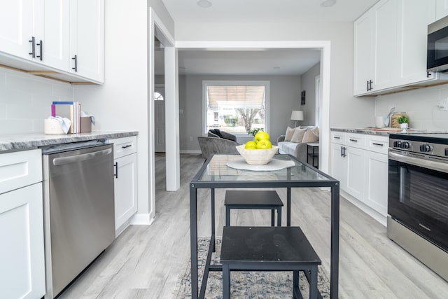 kitchen with appliances with stainless steel finishes, light wood-type flooring, white cabinets, and light stone counters