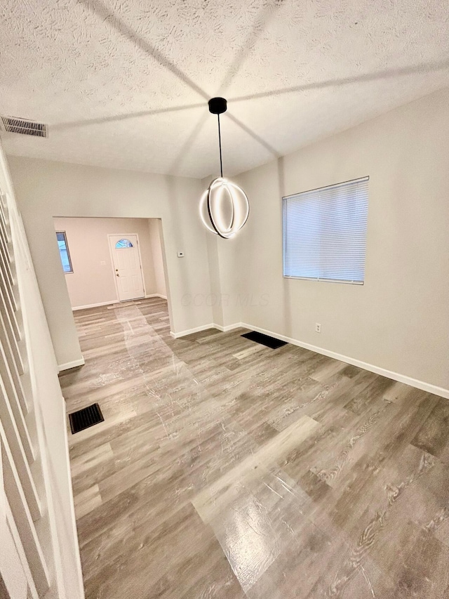 unfurnished dining area with wood-type flooring and a textured ceiling