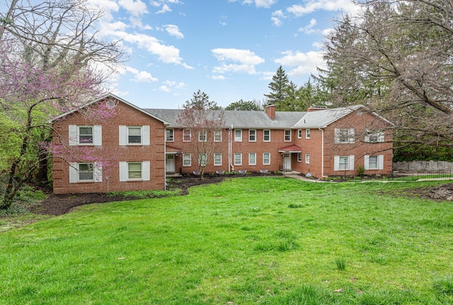 rear view of property with a chimney, brick siding, fence, and a lawn