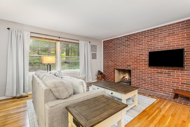 living room featuring brick wall, visible vents, a brick fireplace, and wood finished floors