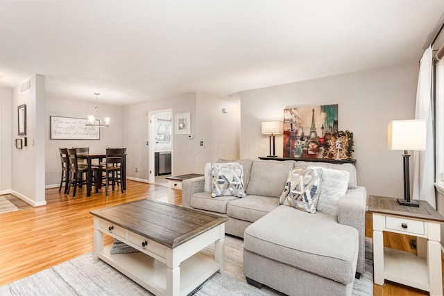 living area featuring visible vents, baseboards, light wood finished floors, and a chandelier
