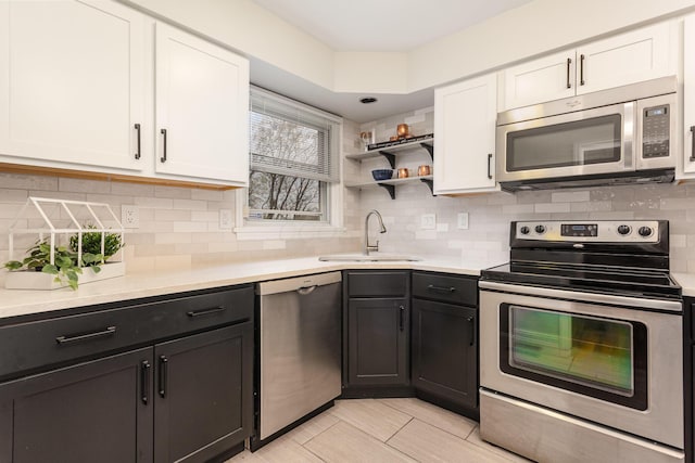 kitchen featuring tasteful backsplash, light countertops, white cabinetry, stainless steel appliances, and a sink