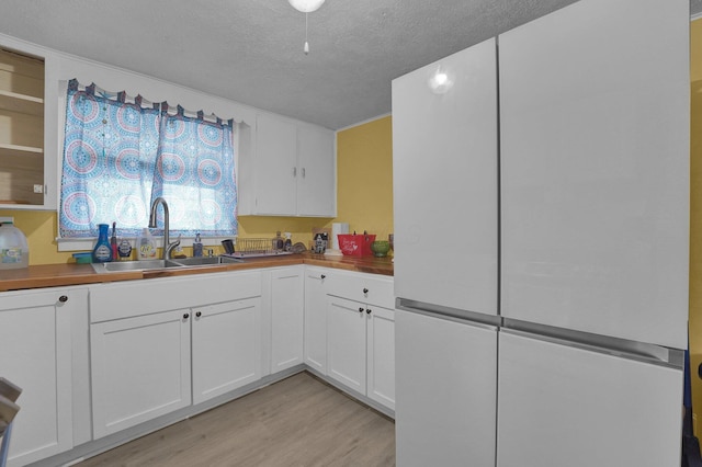 kitchen with butcher block countertops, sink, light wood-type flooring, white refrigerator, and white cabinets