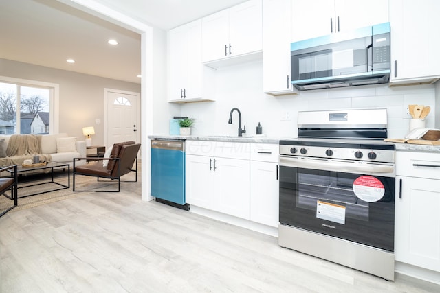 kitchen with sink, appliances with stainless steel finishes, white cabinetry, backsplash, and light wood-type flooring