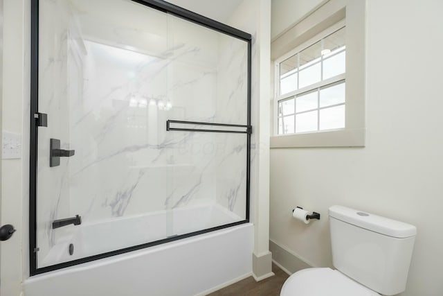 bathroom with toilet and shower / bath combination with glass door