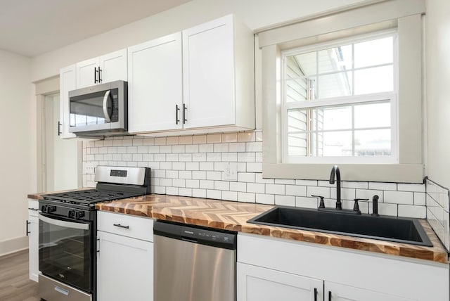 kitchen with butcher block countertops, sink, stainless steel appliances, white cabinets, and decorative backsplash