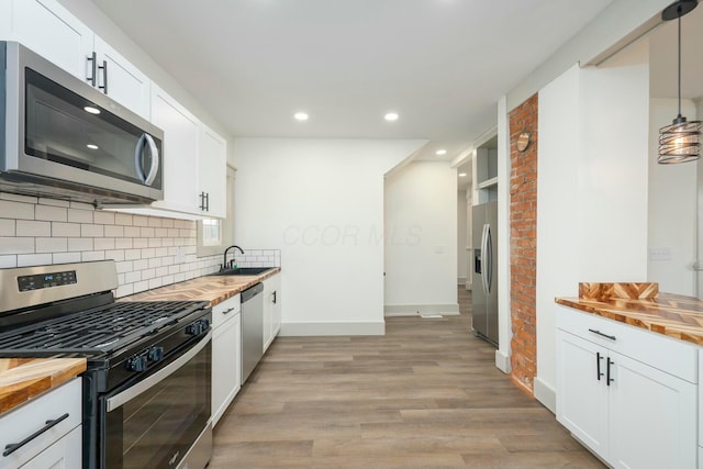 kitchen featuring pendant lighting, white cabinetry, appliances with stainless steel finishes, and butcher block countertops