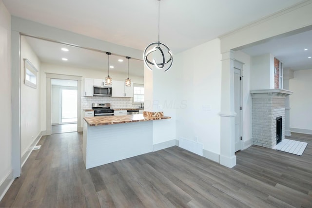 kitchen with white cabinetry, hanging light fixtures, backsplash, stainless steel appliances, and kitchen peninsula