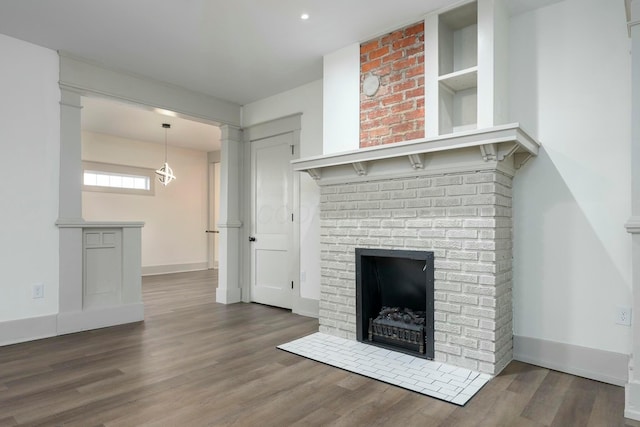 unfurnished living room featuring dark wood-type flooring, a brick fireplace, and ornate columns