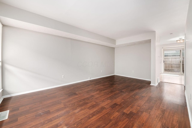 empty room featuring dark wood-style floors, visible vents, and baseboards