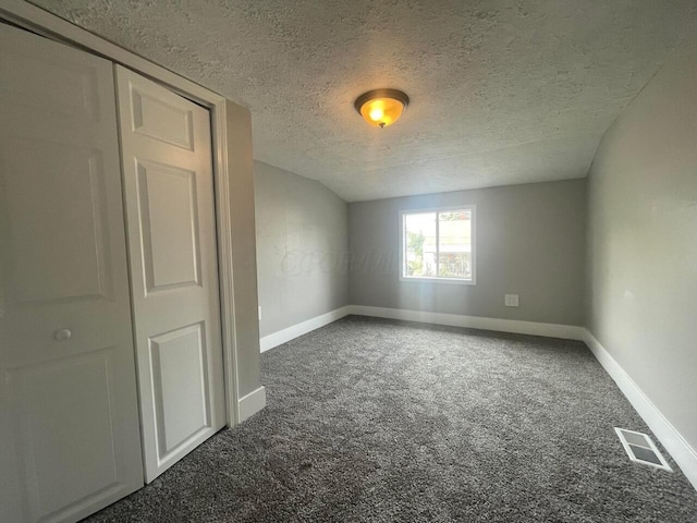 unfurnished room featuring a textured ceiling and dark carpet