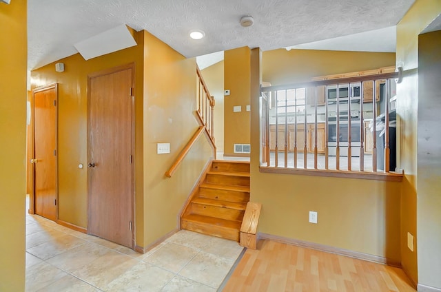 staircase with hardwood / wood-style flooring, vaulted ceiling, and a textured ceiling