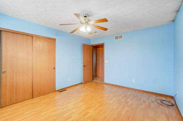 unfurnished bedroom with ceiling fan, light hardwood / wood-style floors, a closet, and a textured ceiling