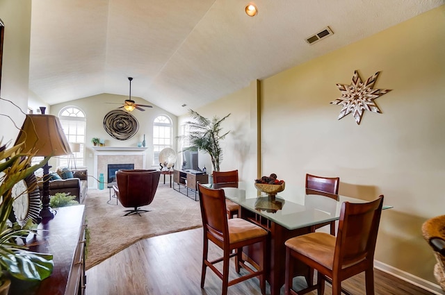 dining room with vaulted ceiling, hardwood / wood-style floors, ceiling fan, and a fireplace