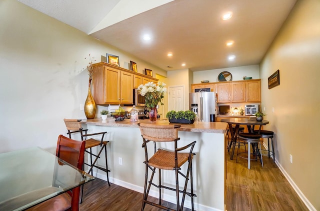 kitchen featuring dark wood-type flooring, high end refrigerator, a kitchen bar, and kitchen peninsula