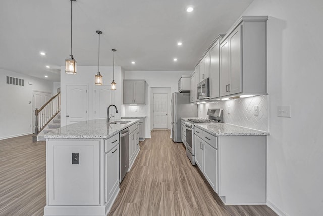 kitchen featuring sink, light stone counters, hanging light fixtures, stainless steel appliances, and a kitchen island with sink