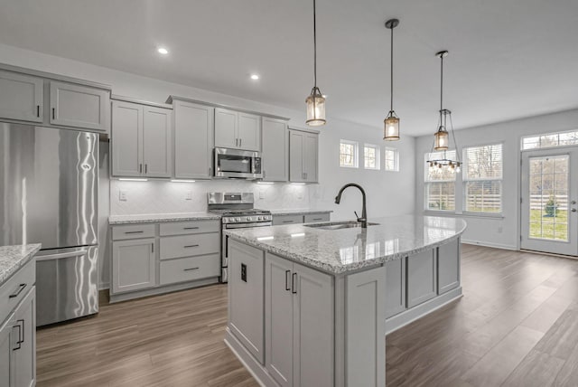 kitchen with pendant lighting, sink, stainless steel appliances, light stone countertops, and a center island with sink