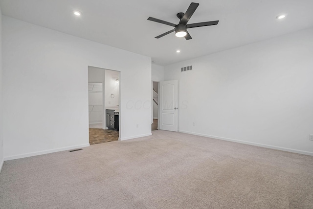 unfurnished bedroom featuring ceiling fan, light colored carpet, and ensuite bath