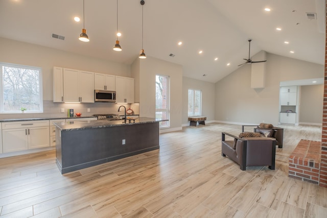 kitchen featuring dark stone countertops, hanging light fixtures, white cabinetry, light hardwood / wood-style floors, and an island with sink