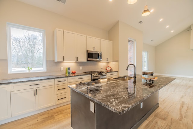 kitchen featuring dark stone countertops, sink, stainless steel appliances, and a center island with sink