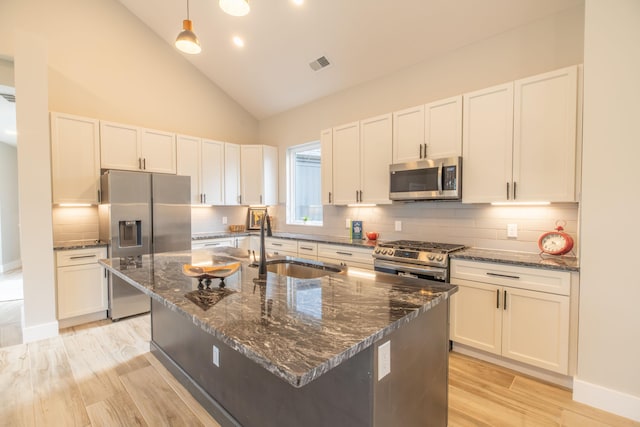 kitchen featuring sink, a kitchen island with sink, stainless steel appliances, white cabinets, and dark stone counters