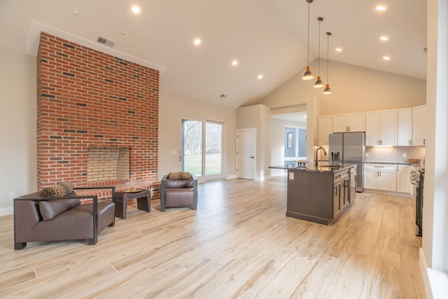 kitchen with stainless steel appliances, pendant lighting, dark stone counters, a kitchen island with sink, and white cabinets