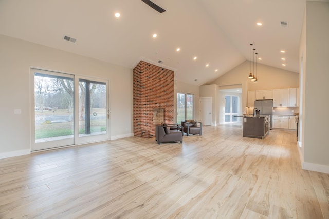 unfurnished living room with sink, high vaulted ceiling, and light hardwood / wood-style floors