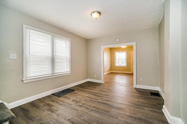 empty room featuring dark wood-style flooring, visible vents, and baseboards