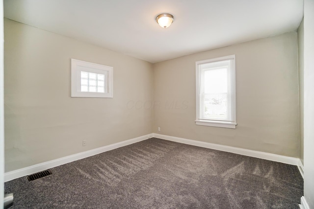 unfurnished room with visible vents, dark carpet, and baseboards