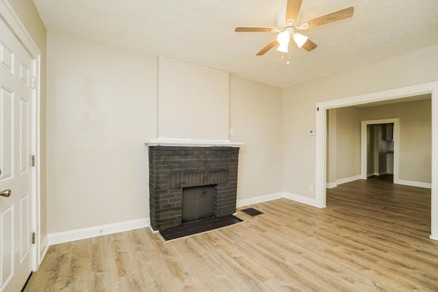 unfurnished living room with a textured ceiling, a fireplace, visible vents, baseboards, and light wood-type flooring