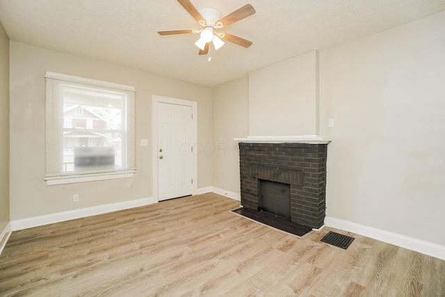 unfurnished living room featuring a brick fireplace, visible vents, baseboards, and wood finished floors