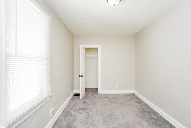 unfurnished bedroom featuring baseboards, carpet, a walk in closet, a textured ceiling, and a closet